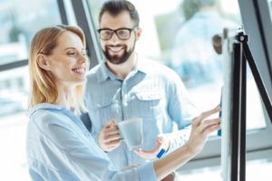 Woman cleaning office white board while talking to a man who holds a cup of coffee